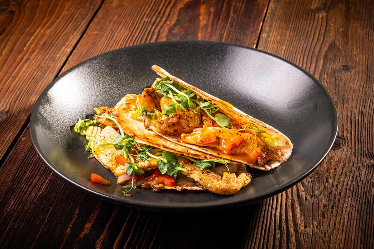 Chicken-Tortillas mit Adis Grillgewürz, Paprika und Currysauce auf schwarzem Teller