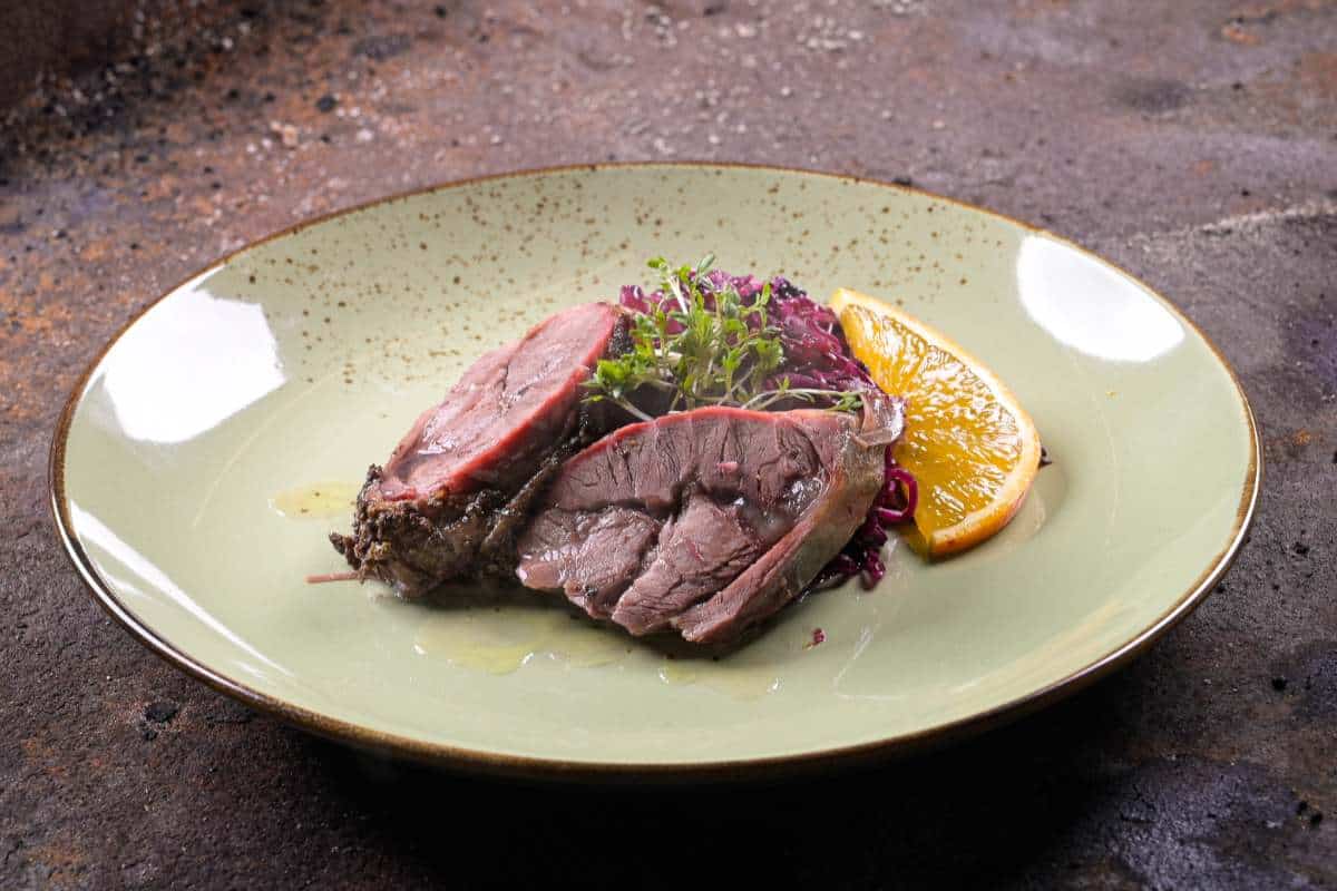 Beef Hammer auf einem Teller mit Rotkrautsalat und Orangenscheibe