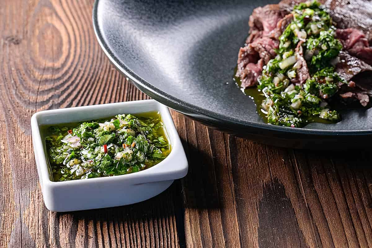 Ein Teller mit einem Steak und einer Schüssel Chimichurri-Sauce.