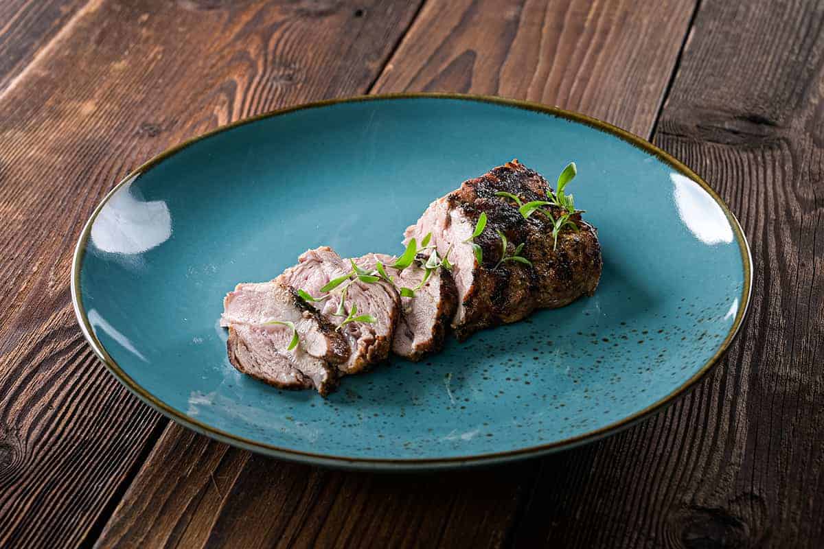 Ein Teller mit Schweinswangerl aus dem Dutch Oven in einer blauen Schüssel auf einem Holztisch.