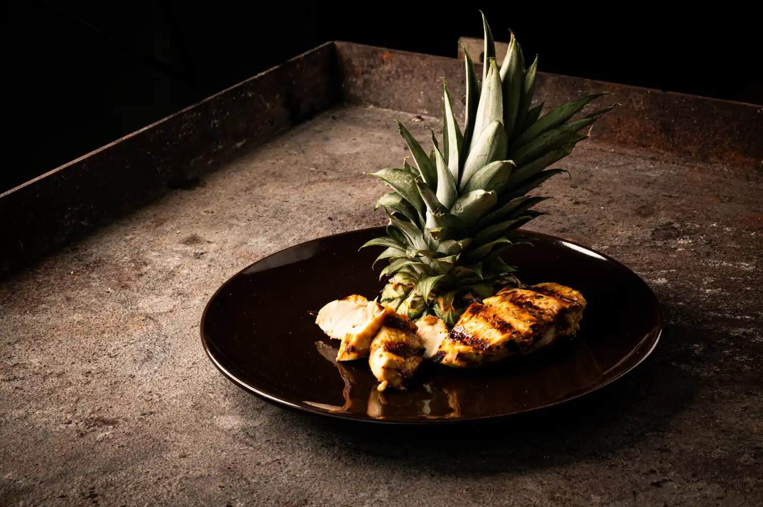 Gegrilltes Hühnerbrustfilet mit frischer Ananas auf schwarzem Teller