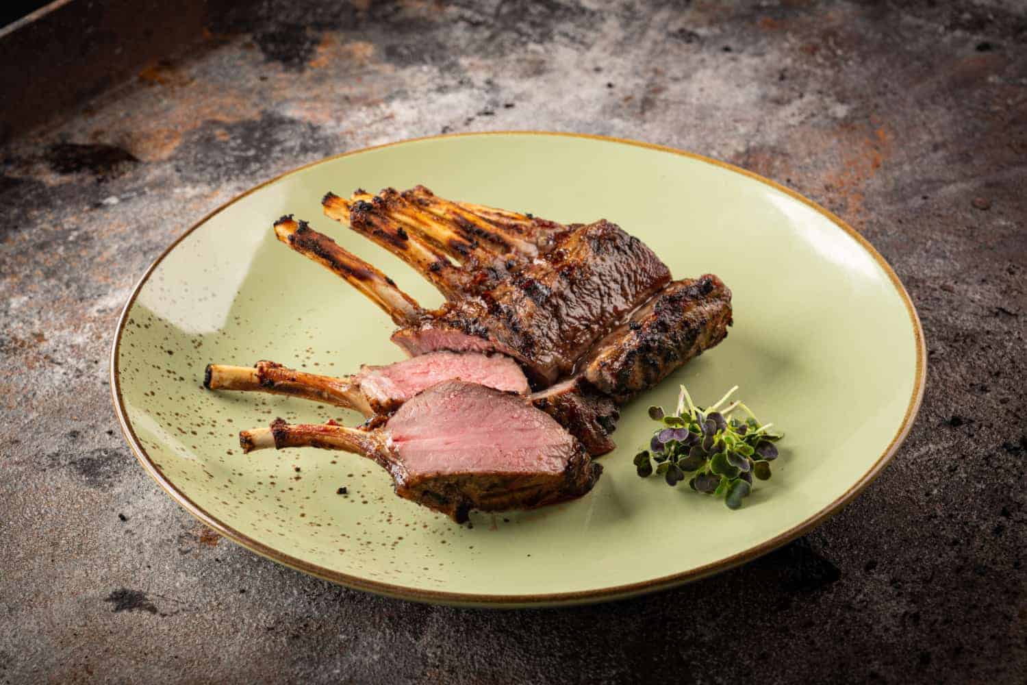 Rosa gegrillte aufgeschnittene Lammkrone auf einem grünen Teller.