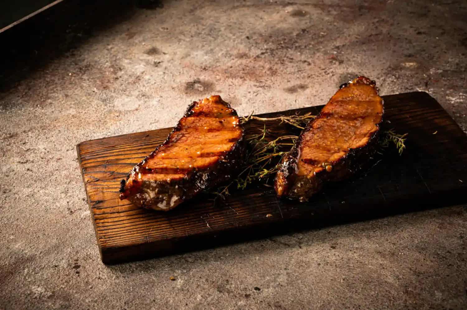 Zwei mit Honig-Miso-Glasur glasierte gegrillte Fleischstücke auf einem Holzbrett mit Thymian
