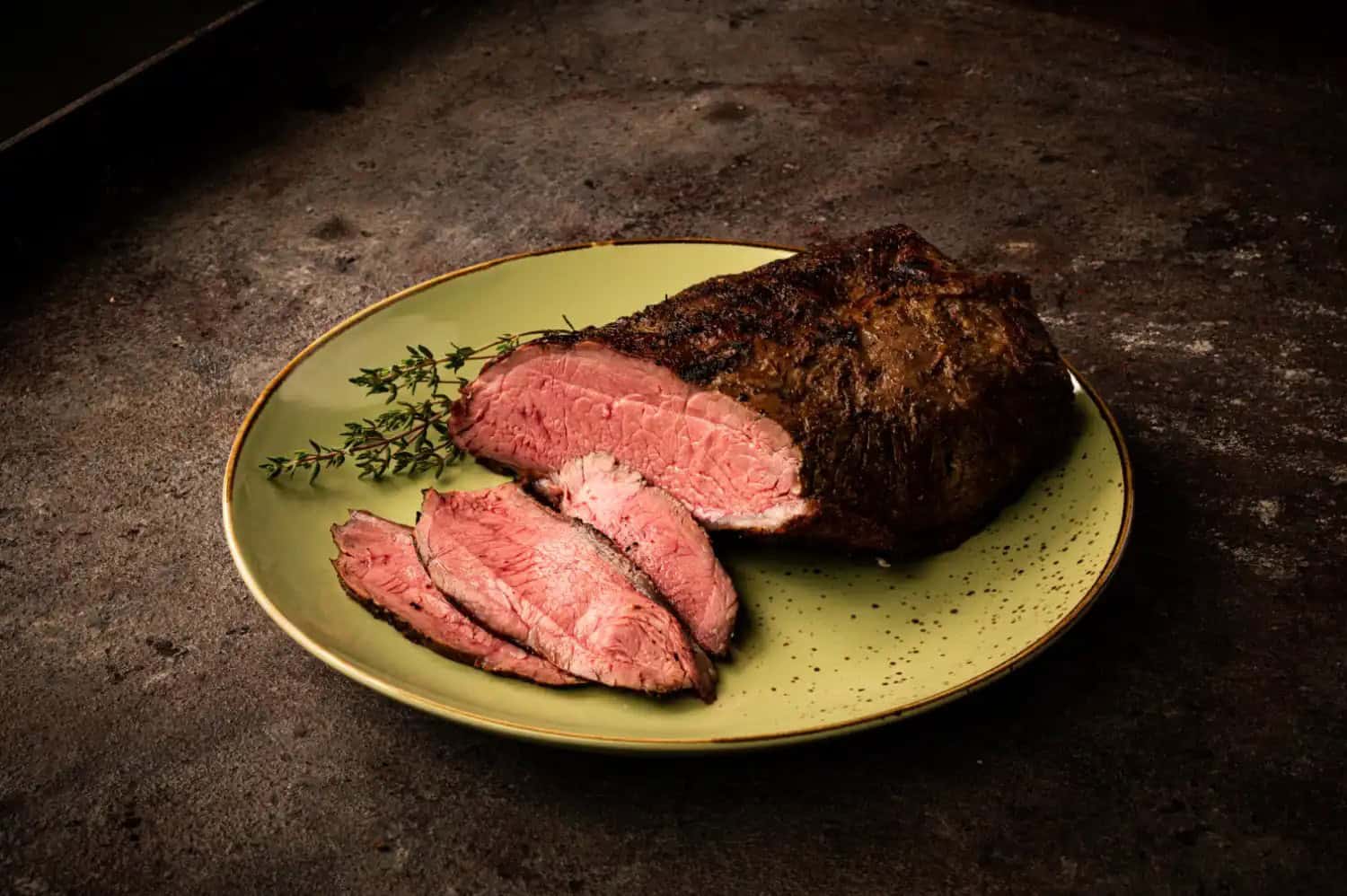Aufgeschnittener rosa gegrillter Kalbstafelspitz mit Thymian auf grünem Teller