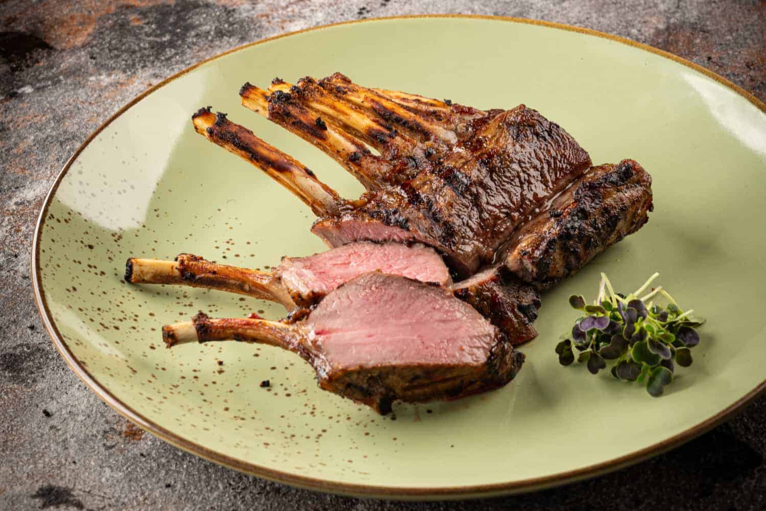 Rosa gegrillte aufgeschnittene Lammkrone auf einem grünen Teller.