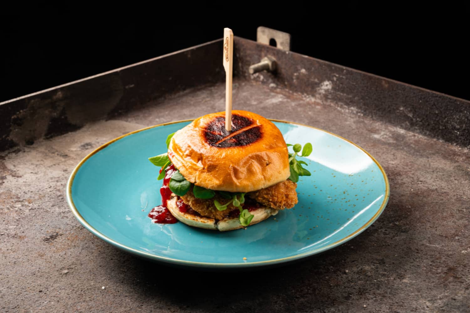 Fledermaus Schnitzel Sandwich mit Vogerlsalat und Preiselbeersauce auf türkisem Teller