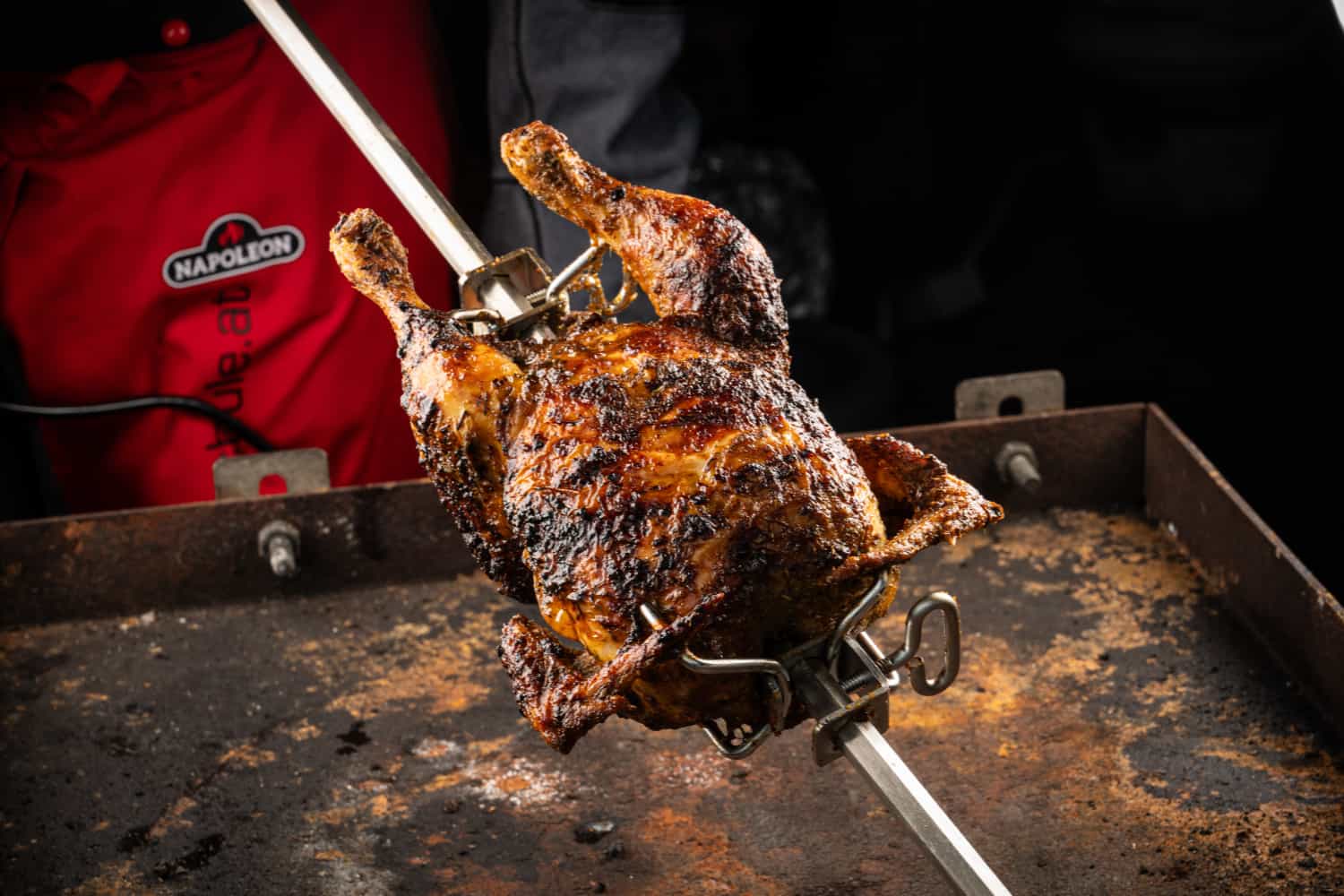 Ganzes Hendl am Drehspieß über dem Grill, knusprig braun gebraten.
