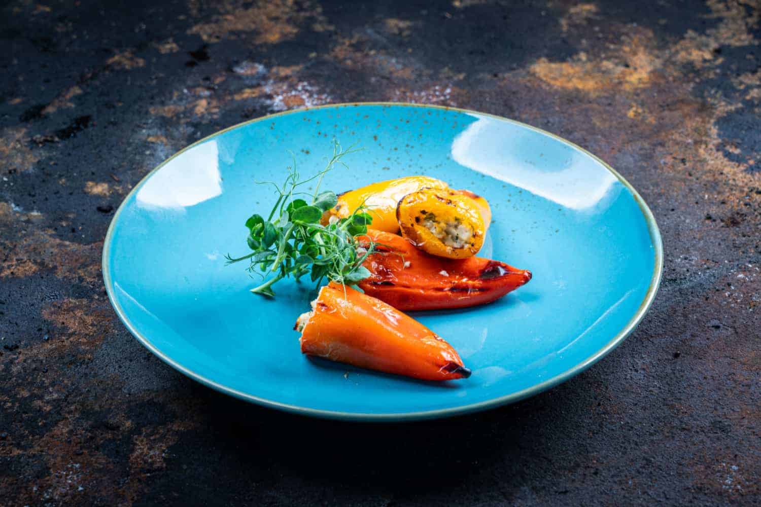 Gefüllte Spitzpaprika mit Feta und Frischkäse vom Grill, serviert auf einem blauen Teller mit Mikrogrün.